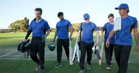 Cricket team walking off field in blue jerseys carrying bats and helmets
