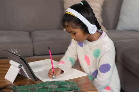 Asian girl studying at home writing in notebook with tablet and headphones, concentrating