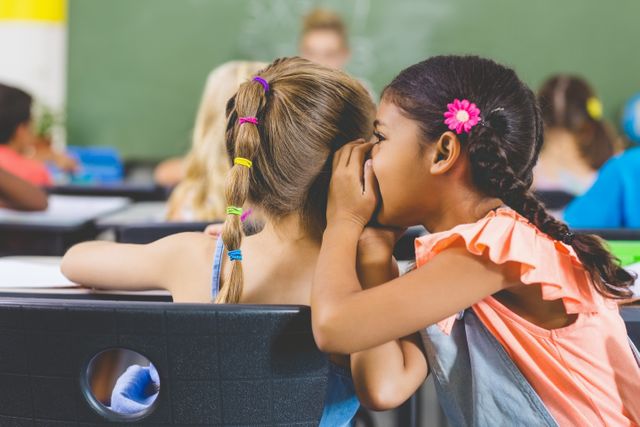 Schoolgirl whispering into her friend s ear in classroom - Download Free Stock Photos Pikwizard.com