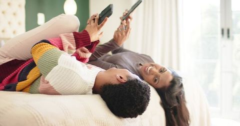 Smiling Female Friends Relaxing with TV Remotes on Bed