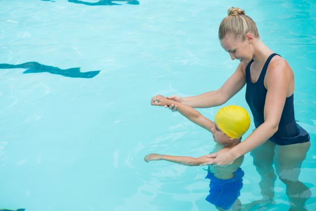 Female instructor training young boy in pool. Ideal for content related to swimming lessons, water safety, child education, and aquatic activities. Useful for promoting swim schools, leisure centers, and summer programs.