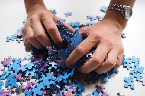 Hands Sorting Colorful Puzzle Pieces on White Surface