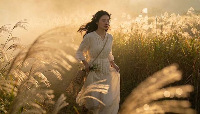 Golden hour woman walking through tall grass in flowing white dress carrying flower basket