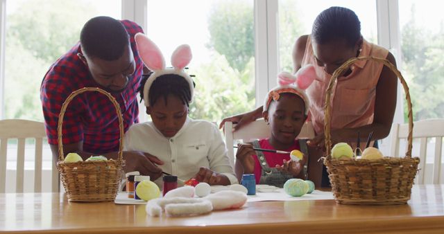 Family decorating Easter eggs together indoors, wearing bunny ear headbands and enjoying time doing crafts. Ideal for use in content about family bonding, holiday celebrations, creative activities with children, and Easter traditions.