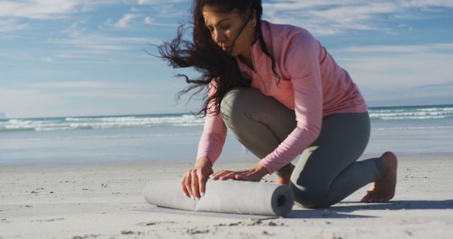 Biracial woman rolling yoga mat at the beach. healthy active lifestyle, outdoor fitness and wellbeing.