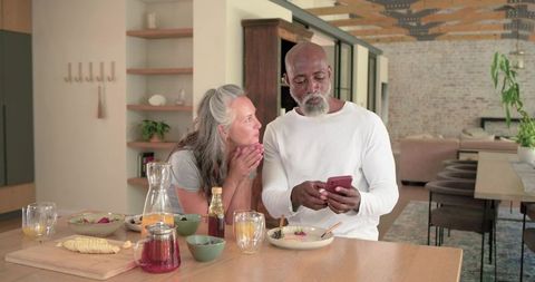 Mature couple sharing breakfast while using smartphone in modern open-plan kitchen