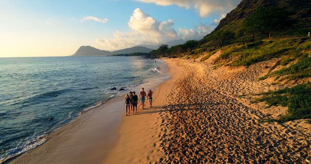 Depicts a group of people enjoying a calm walk on a sandy beach with the sun setting. Ideal for use in travel promotions, vacation brochures, advertisements for beach resorts, and nature blogs focusing on travel, adventure, and relaxation.