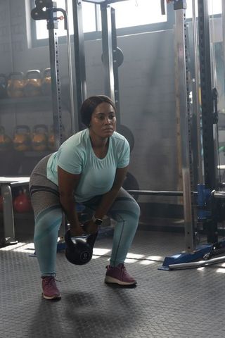 African american woman performing kettlebell swing in industrial gym for strength training