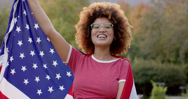 Captivating depiction of a young woman holding an American flag outdoors, embodying national pride and happiness. Ideal for promoting patriotism, advertising Independence Day events, or illustrating concepts related to celebration, freedom, and national identity. Can be used in campaigns, social media posts, articles about citizenship, or educational materials.