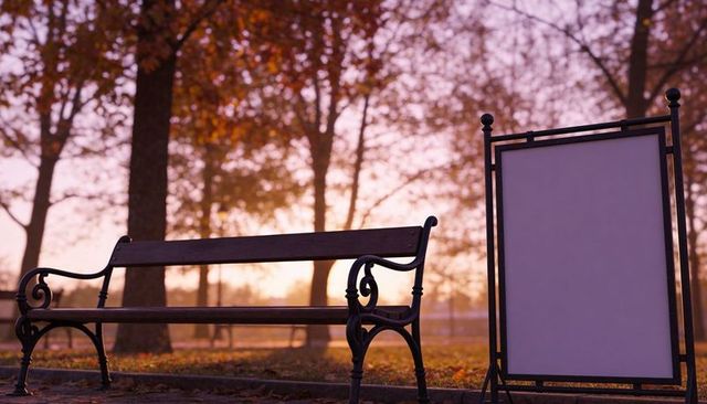 Empty wooden park bench basking in golden autumn sunset with blank signboard