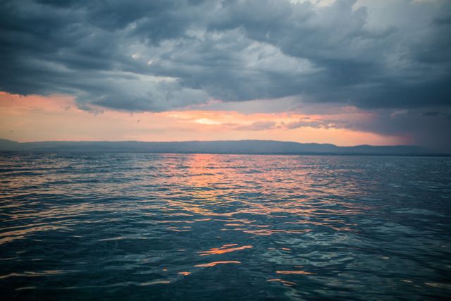 Beautiful image capturing the serene moment of a sunset over a calm ocean with dramatic clouds covering the sky. Ideal for use in nature-themed projects, travel brochures, or calming background art.