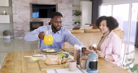 Diverse Couple Pouring Orange Juice at Cozy Breakfast Table in Bright Modern Living Room