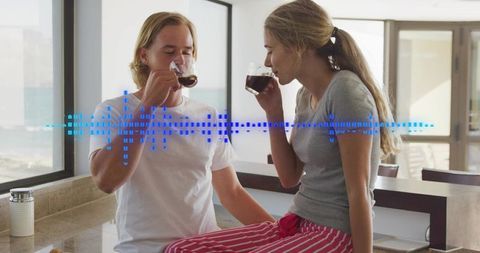 Young couple sipping coffee in bright kitchen with digital waveform overlay
