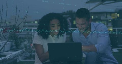 Young Professionals Collaborating on Laptop at Rooftop Dusk with Data Overlay