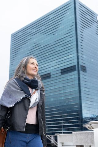 Mature woman looking up by glass high-rise carrying leather bag urban professional lifestyle