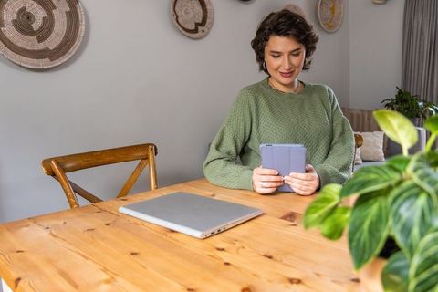 Woman in green sweater holding tablet at wooden dining table for remote work lifestyle