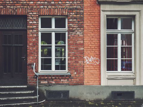 Urban brick facade showing vintage sash windows, dark wooden door and graffiti accent