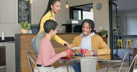 Diverse friends enjoying coffee at cozy cafe while barista handing white plate
