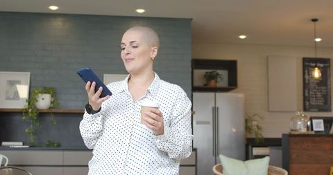 Woman checking smartphone while holding coffee cup in modern kitchen cafe workspace