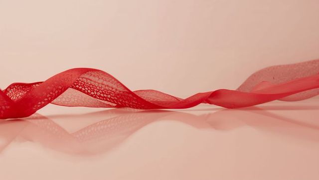 Flowing red lace ribbon creating mirror reflection on glossy pink surface minimal texture