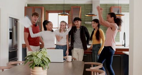 Young Adults Celebrating Virtual Win at Kitchen Island Around Laptop During Home Gathering