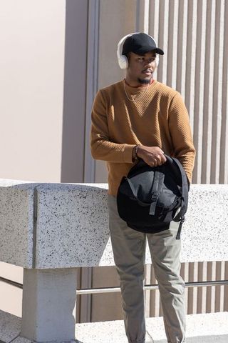 African american man standing on rooftop terrace holding backpack wearing headphones