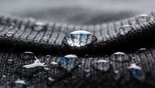 Macro water droplets beading on charcoal knit seam showing iridescent blue reflections