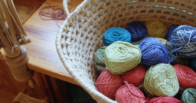 Close-up view of a woven basket filled with colorful yarn balls placed on a wooden surface. Ideal for use in articles, blog posts, and promotional materials related to knitting, crochet, DIY crafts, and textile arts. Evokes creativity, warmth, and the joy of handmade crafting.
