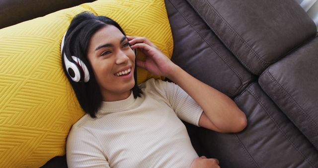 A woman enjoying music with headphones while comfortably relaxing on a couch. Useful for depicting leisure, relaxation at home, casual lifestyle, and enjoyment of music. Ideal for advertising home decor, music streaming services, headphones, and stress-free living.