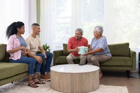 Grandparents giving gift to expecting couple in sunlit living room