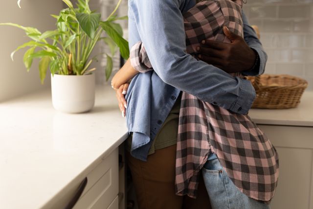 Young couple embracing in a modern kitchen, showcasing love and togetherness. Ideal for use in lifestyle blogs, relationship advice articles, home decor websites, and advertisements promoting romantic or home-related products.
