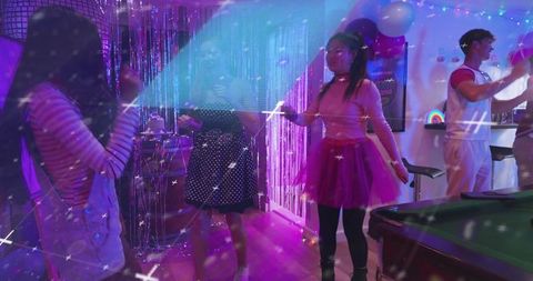 Friends dancing in neon party room with pink tutu, metallic backdrop, pool table