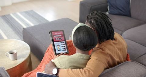 African American couple shopping online on tablet while cuddling on cozy gray sofa