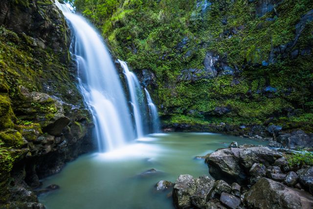 This image features a majestic waterfall cascading into a pool of water surrounded by lush green foliage and moss-covered rocks. Ideal for travel brochures, nature magazines, relaxation therapy visuals, desktop wallpapers, or any project promoting tranquility and natural beauty.