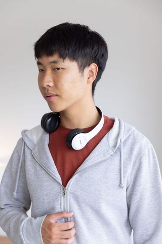 Young asian man wearing headphones adjusting hoodie zip in minimalist room