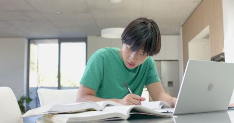 Focused Asian Male Student Taking Notes with Laptop