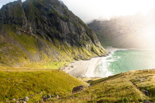 Image capturing a stunning coastal landscape in the Lofoten Islands of Norway. This beach is backed by dramatic mountains, with waves crashing onto the shore and sunlight peeking through. Perfect for use in travel guides, outdoor adventure promotions, and nature-inspired designs.