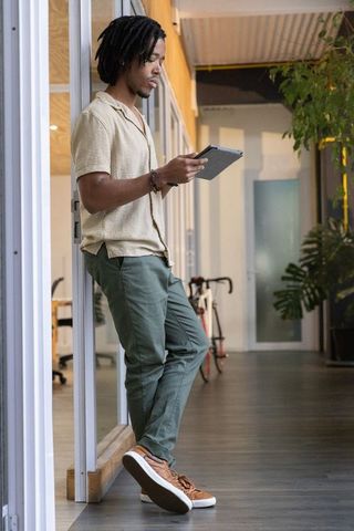 African american man leaning on glass wall reading tablet in modern coworking corridor