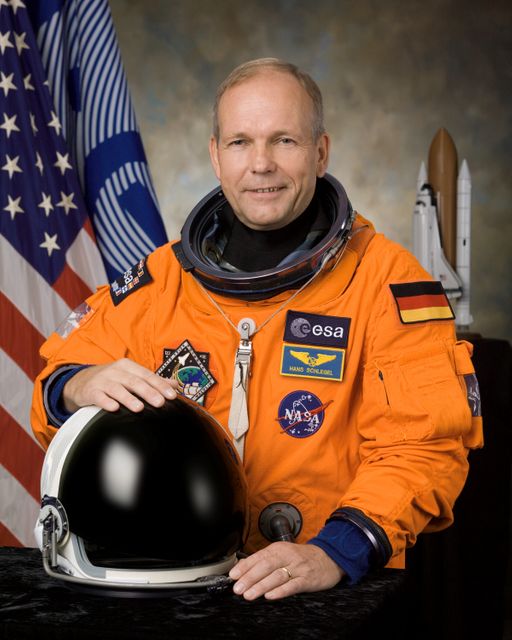The image depicts an astronaut in an orange spacesuit, posing with a black helmet, in front of flags from the European Space Agency (ESA) and NASA. Suitable for content related to space missions, astronaut training, ESA and NASA collaborations, space exploration, and educational material.