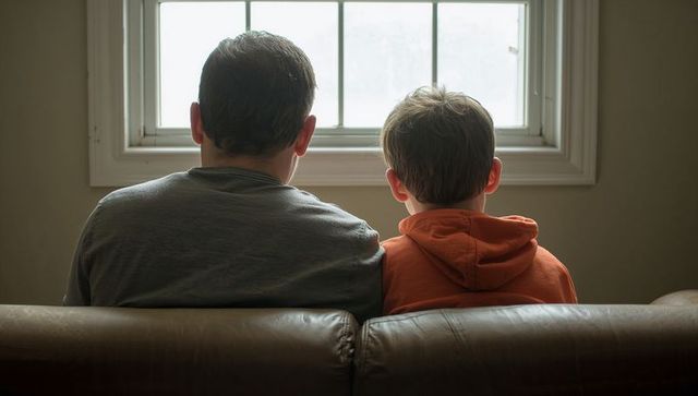 Parent and child sitting on couch looking out window, quiet reflective home moment