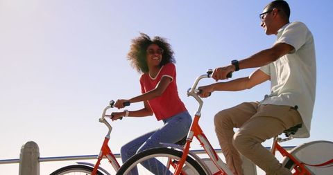 Joyful mixed-race couple cycling on beach promenade