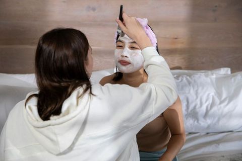 Diverse Women Applying Facial Mask for Relaxation in Cozy Bedroom