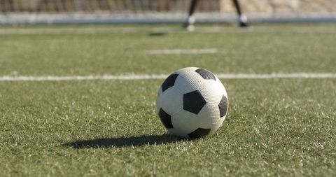 African american teen goalkeeper standing behind soccer ball on artificial turf close-up