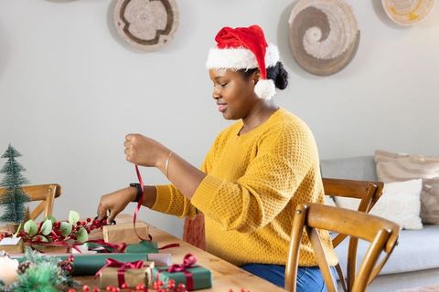 African american woman wearing santa hat wrapping christmas gifts at rustic wooden table