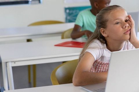 Bored schoolgirl resting head during laptop lesson in bright classroom