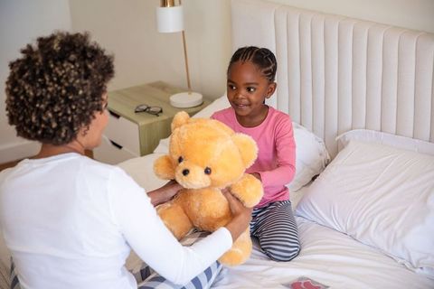 Child with mother enjoy playtime on bed with teddy bear