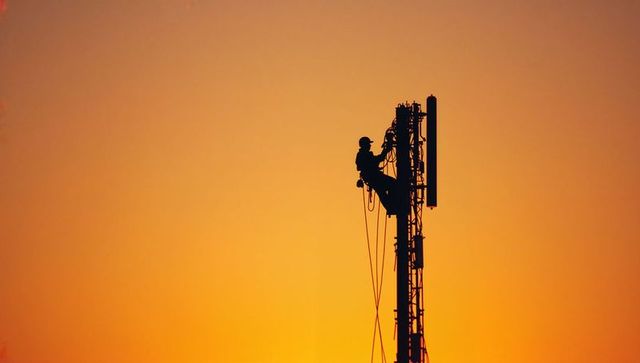 Technician Climbing Tower with Antennas at Dusk Silhouette