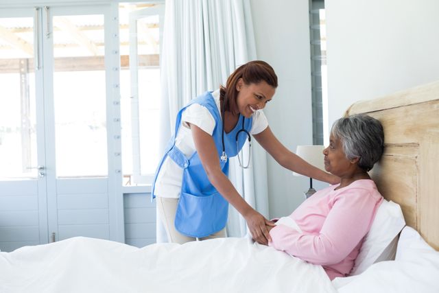 Female doctor comforting senior woman in bed at home. Ideal for use in healthcare, elderly care, and home care service promotions. Highlights compassion and support in medical care settings.