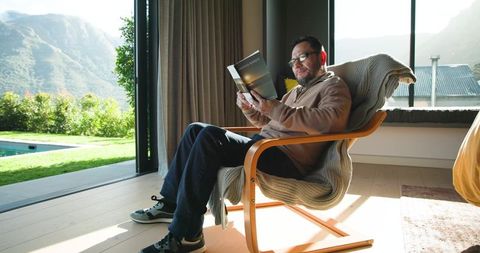 Senior Asian Man Relaxing Indoors while Reading in Sunlit Room