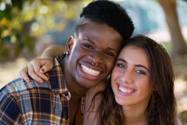 The couple is smiling and embracing outdoors, portraying a joyful and loving relationship. This image can be used for content related to friendship, love, diversity, and positive emotions. Ideal for advertisements, social media posts, and articles promoting togetherness and happiness.